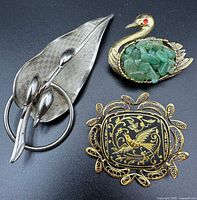 Front view of three brooches: damascene square, swan with jade chips, leaf brooch