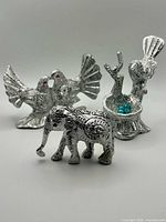 Front view of all three silver-tone metal figurines: elephant, kissing doves, bird on nest
