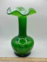 Full view of green hand-blown glass vase with ruffled rim, trumpet neck and bulbous base beside ruler