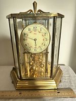 Full front view of Kundo anniversary clock showing dial, pendulum, base and glass panels