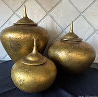 Three gold-tone jars with lids displayed together