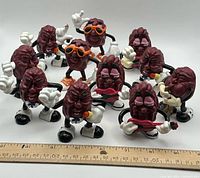 Group shot of 11 California Raisins figurines in various poses with ruler for scale