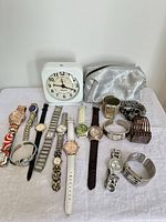 Group view of all wrist watches, Westclox alarm clock and silver pouch on table