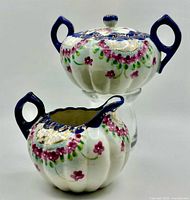 Sugar bowl with lid stacked on glass stand above matching creamer, showing overall form and decoration