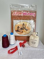 Group shot of sealed cross-stitch kit, thread cones, zippers, fabric rose and rock salt bag