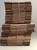 Stacked bundles of flat brown corrugated cardboard boxes strapped together