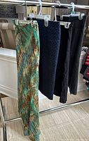 Four skirts hanging on garment rack: green/teal sequin watercolor, navy pin-dot, black linen, gray pinstripe
