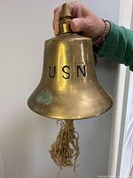 Front view of brass bell showing USN marking and rope tassel