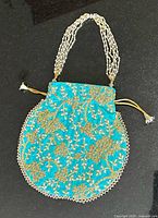 Full view of turquoise potli bag showing embroidery, handle and drawstring