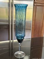 Full view of tall blue handblown glass hurricane vase on countertop