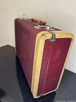 Side view of burgundy suitcase showing tan edging, handle, and latches