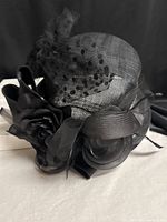 Front view of black wide-brim hat showing flower, ribbon loops and dotted veiling bow