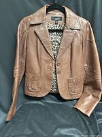 Full view of brown leather jacket on hanger