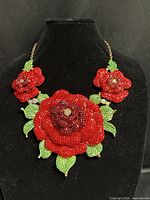 Full necklace on display bust showing three red crystal roses with green leaves and gold-tone chain