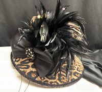 Hat front angle showing leopard print fabric, feather spray, satin bow and rhinestone brooch