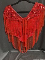 Full view of red sequin shawl on hanger showing front drape and fringe length