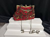 Front view of red beaded clutch showing metal frame, ornate handle and chain