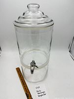 full view of glass beverage dispenser with lid and spigot beside 12-inch ruler