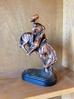 Front left view of bronze finish cowboy on bucking horse statue showing full pose and base