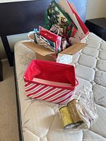Cardboard box containing multiple gift bags, striped fabric bin in foreground, plastic-wrapped ribbon spools beside