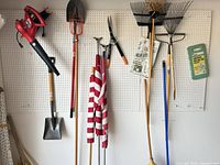 Overall view of tools on pegboard including blower, shovels, rakes, broom, shears, kneeler and flag