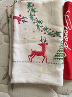 Folded white linen runner showing red cross-stitch reindeer and holly border