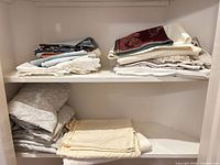 Two shelves with folded linens: patterned sheets, cream sheets, tablecloth stacks