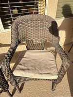 Front view of one brown resin wicker armchair with beige cushion