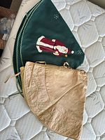 Two tree skirts folded, showing green Santa design and gold satin skirt