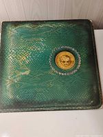 Front of green snakeskin gatefold sleeve with gold medallion