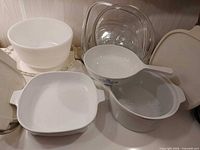 Assorted white CorningWare dishes, Hamilton Beach bowl, clear glass Pyrex lids and beige plastic lids displayed together