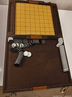Open case showing yellow grid Go board, felt surface and numerous black and white stones