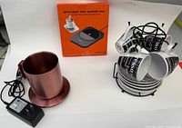 Lot overview with sealed mug warmer pad box, copper Ember mug with coaster and adapter, espresso cup set on rack