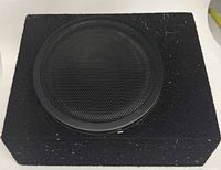Top view showing circular metal speaker grille set into black carpeted enclosure