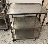 Full view of stainless steel cart showing three shelves, handle, casters