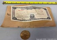 Certificate on aged envelope with coin below, measuring tape for scale
