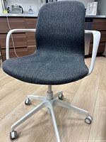 Front view of grey upholstered swivel office chair showing seat, back, armrests, white five-leg base with casters