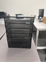 stack of six black metal mesh desk paper trays on tabletop