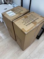 Two sealed cardboard boxes of PPE gowns standing side by side