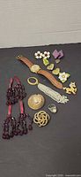 Entire lot laid out showing watch, necklaces, brooches, ring, tassel and assorted earrings