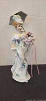 Full view of porcelain lady figurine showing parasol, gown, bouquet