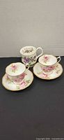 Group shot showing two American Beauty cup and saucer sets and one Flower of the Month February teacup