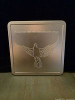 Lid of square metal case showing engraved dove motif and text