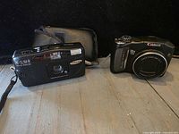 Front view of Samsung AF Slim R film camera, Canon PowerShot SX120 IS digital camera, and soft case