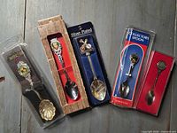 Five packaged silver-plated souvenir teaspoons displayed side by side