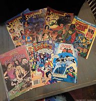 Seven assorted comic books and magazines arranged on tabletop: three Superman & Batman issues, Amazing Spider-Man book and record set, Untold Legend of the Batman, Archies, Poison