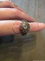 Ring on finger showing flower face with clear central stone and rhinestone petals