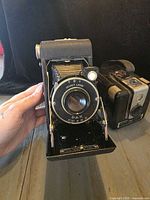 Front view of Kodak Vigilant folding camera with bellows extended; partial view of Brownie Hawkeye in background