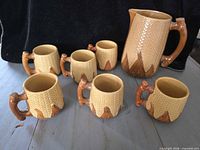 Pitcher and six matching corn cob mugs displayed on tabletop