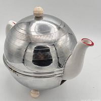 Side view of aluminum tea cosy enclosing ceramic teapot